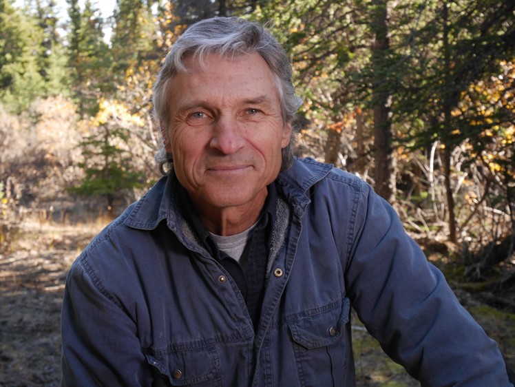 Dr Boutin, a man with short wavy gray hair, in front of a forest wearing a blue jean button-down shirt.