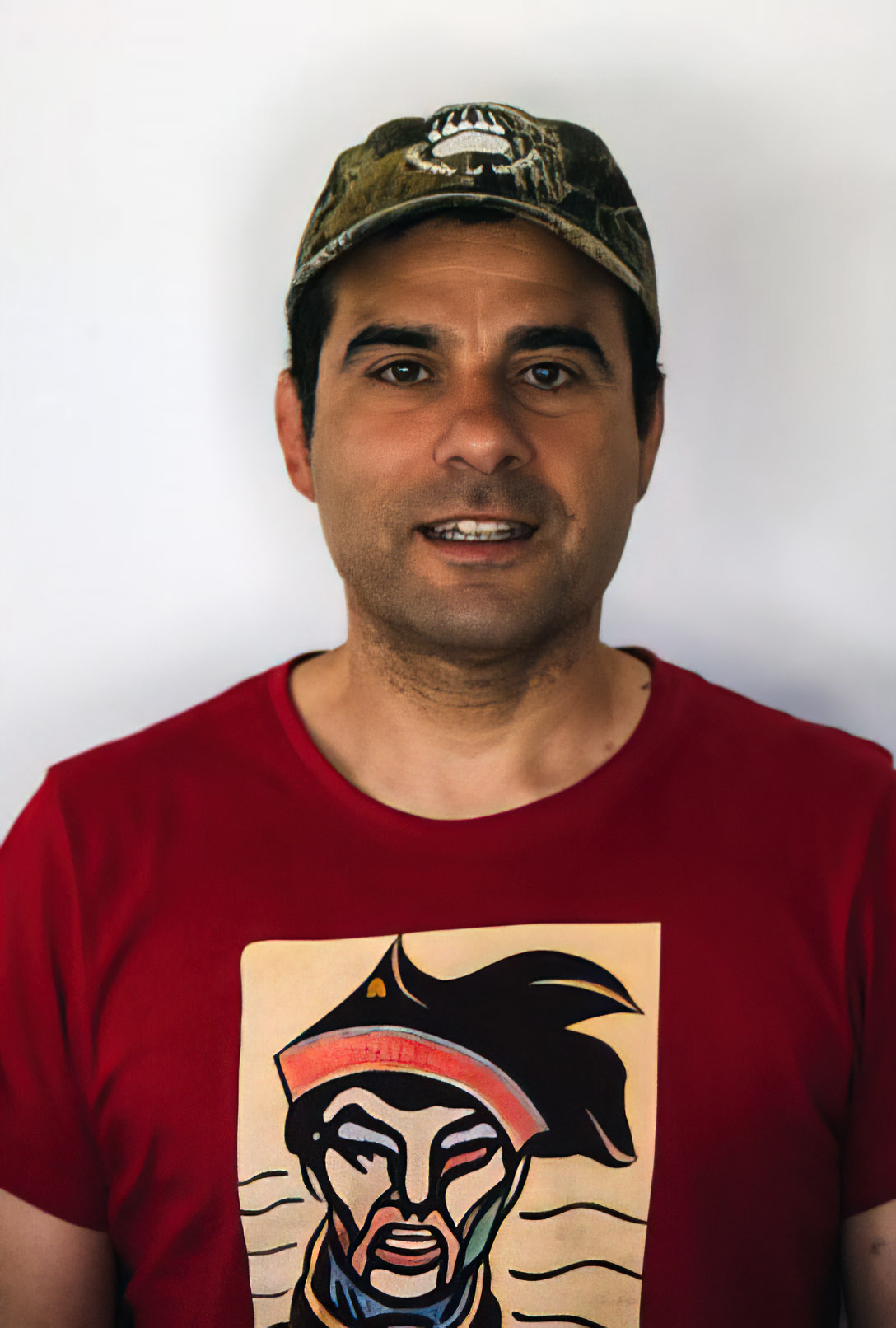 Dr. Robert Serrouya, a man with short hair, standing in front of a white backdrop, wearing a graphic t-shirt and a camo baseball cap.